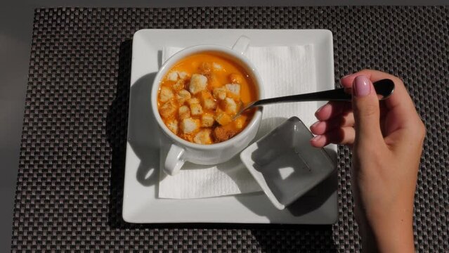 Woman stir dry bread cubes with Gazpacho soup, start eating popular Spanish meal at cheap cafe at lunch time. Top view of square plate with small bowl of liquid cold soup