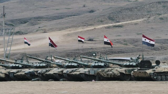 Tanks with Syrian flags lined up in hilly area. Armoured fighting vehicles guard and protect borders of country, ready for offensive or defense. Modern military forces in mountain place