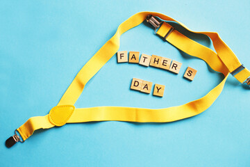 happy father's day lettering made by wooden cubes on a blue background with a yellow suspenders