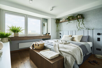 Stylish bedroom interior in modern apartment with small bed, wooden chest, home garden, white...