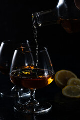 Two cognac glasses on a dark background. Cognac is poured into one glass from above