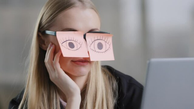 Tired female unmotivated manager with stickers on eyes sitting at desk sleeping at workplace chronic fatigue lazy businesswoman in office exhausted napping relaxing with sticky notes on eyeglasses