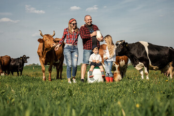 Happy farmers family in green field with big cow in a green field with flowers on a sunny summer day