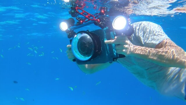 Photographer with underwater housing turns around towards the camera and takes picture