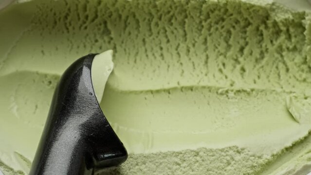 Green ice cream scooped out of container by spoon. Top view of pistachio ice cream. Delicious dessert. Food concept. Yummy. Close-up in 4K, UHD