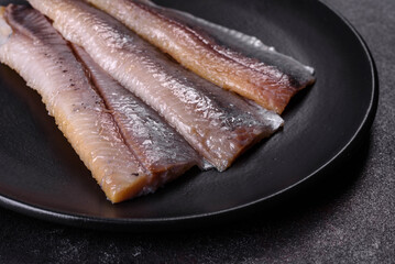 Delicious fresh herring fillet with salt, spices and herbs on a black plate