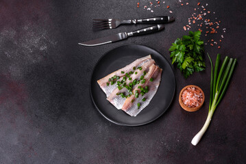 Delicious fresh herring fillet with salt, spices and herbs on a black plate