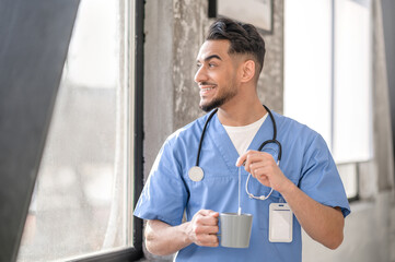 Pleased physician brewing tea by the window