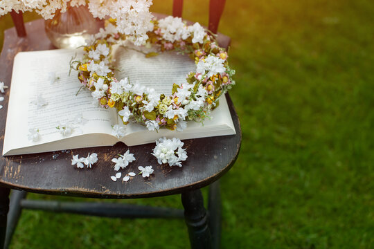 a book, a wreath and a bouquet of white lilac as a composition on an old chair in a sunny garden