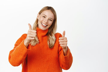 Portrait of smiling blond attractive woman, showing thumbs up in approval, like or recommend,...
