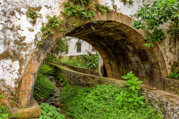 Old historical stone tunnel passing through vegetation and old colonial-style houses in the historic city of Ouro Preto in the state of Minas Gerais.
