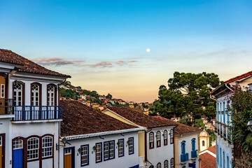 Fototapeta na wymiar Old colonial style houses with their balconies in the traditional historic town of Ouro Preto during sunset with the moon in the background