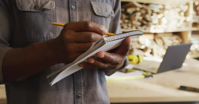 Mid section of african american male carpenter taking notes in a carpentry shop