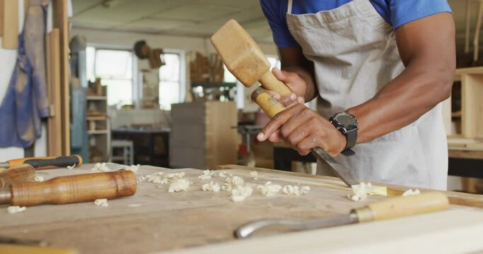 Mid section of african american male carpenter carving wood with hammer and chisel at carpentry shop