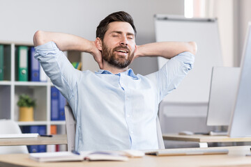 Young handsome man, office worker, sitting at a computer desk, stretching, tired, taking a break, doing yoga exercises, resting