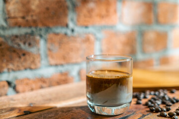 A Glass of Dirty coffee by espresso shot topped over cold fresh milk create a gradient layer in the morning over a red bricks wall background and coffee beans on a wooden Cafe table. For Copy Space