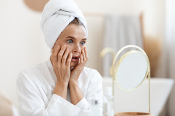Shocked middle aged woman looking at mirror, touching her skin