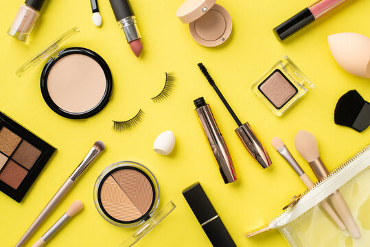 Make up concept. Top view photo of compact powder eyeshadow contouring palette nail polish brushes lipstick false eyelashes beauty blenders mascara lip gloss cosmetic bag on isolated yellow background