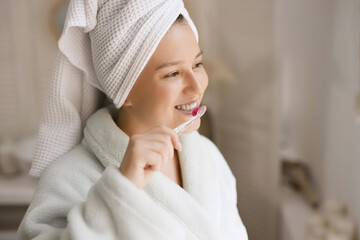 Young girl brushing her teeth in the bathroom. Model with natural nude make up with towel on head.