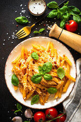 Italian pasta with tomato sauce, basil and parmesan cheese on dark table.
