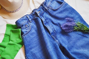 Trendy summer women's clothes flat lay photography. Hat, blue jeans, green socks and lavender flowers. Stylish modern outfit with denim clothing