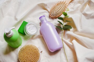 Green liquid soap package, moisturizing cream jar, purple shampoo bottle, massage brush, wooden comb and eucalyptus leaves flat lay beauty photography. Organic cosmetic for skin and hair care