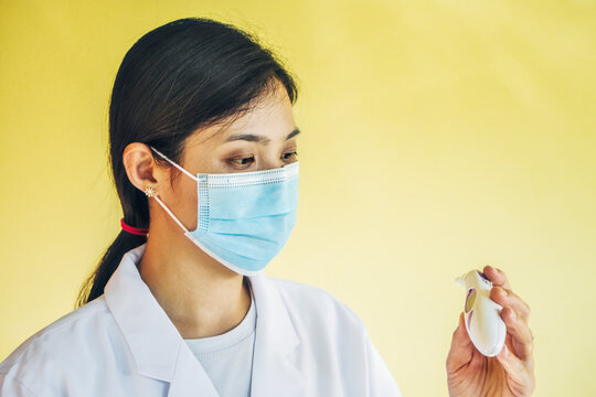 Closeup Of Nurse Reading Infrared Thermometer Against Yellow Background.