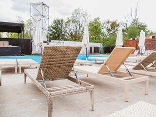 Rattan reclining chaise. Comfortable outdoor patio wicker chaise lounges. Swimming pool backyard resort furniture. Empty chairs in hotel with sunlight on sunny day.