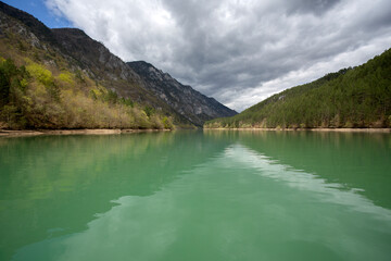 Cruise on the river Drina. The beautiful green waters reflect the mountain hills and the cloudy sky.