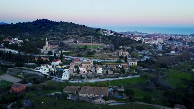 unique aerial drone shot of Badalona Barcelona, Spain where we see the mountains with leafy trees, vegetation of the small town with amazing sunset lighting and the roads and beach at background