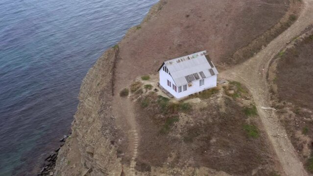 House of hermit is on mountain cliff on sea coast. Top, aerial view. Home of anchoret, recluse, loner, isolato standing alone on rock near ocean shore. Building isolated from another world on hill