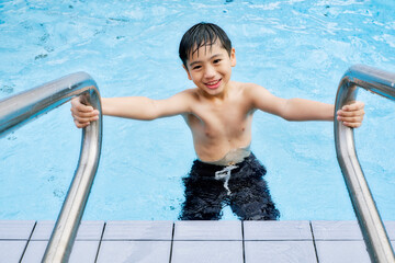 Kid holding on the handrail of an outdoor swimming pool