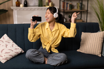 Obraz premium Excited Asian lady listening to music in headphones and dancing