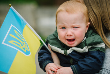Child crying. Sad little boy hugs mom with flag Ukraine in hands. Evacuation of civilians....