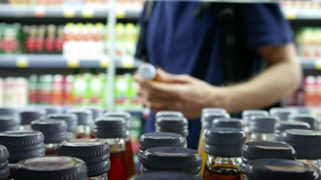 Close-up of many glass bottles of juice with metallic caps on a supermarket shelf and a man takes one