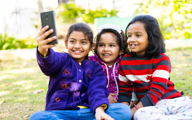 Young girl kids busy making video call on mobile phone at park - concept of social media, technology, internet and childhood friendship