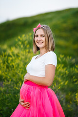 A pregnant woman in a beautiful pink dress walks in a field of flowers and enjoys her pregnancy.