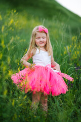 The little girl in a pink dress walks barefoot on the green grass in the field.