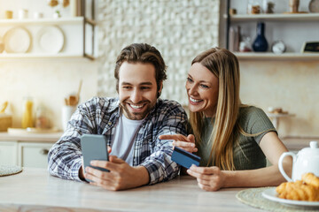 Obraz na płótnie Canvas Smiling surprised caucasian millennial man with stubble and blonde lady with smartphone and credit card