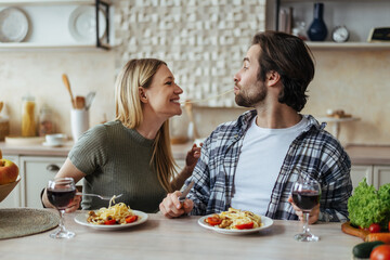 Glad happy handsome caucasian millennial couple eat pasta together, have fun in light kitchen...