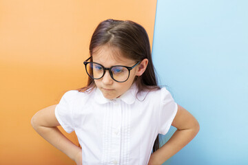 A 7-year-old girl with glasses with an angry face and hands on her sides. Children's education,...