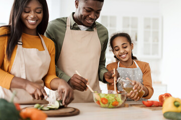 Happy Black Family Cooking Dressing Salad With Oil In Kitchen