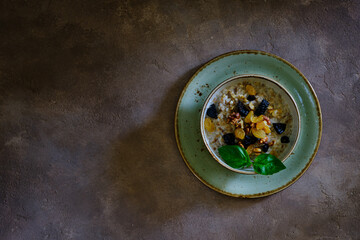Buckwheat porridge with walnut, raisins and prunes on a green plate on a brown background under concrete.