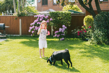 Little girl blowing soap bubbles and playing with the dog on a green lawn in the garden. Having fun...