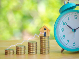 Hand are stacking coins with alarm clock to save the financial stability for the future. Concept for loan, property ladder, financial, mortgage, real estate investment, taxes and bonus.