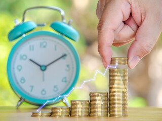 Hand are stacking coins with alarm clock to save the financial stability for the future. Concept for loan, property ladder, financial, mortgage, real estate investment, taxes and bonus.
