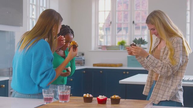 Group Of Teenage Girls Eating And Having Fun Playing With Cupcakes In Kitchen At Home