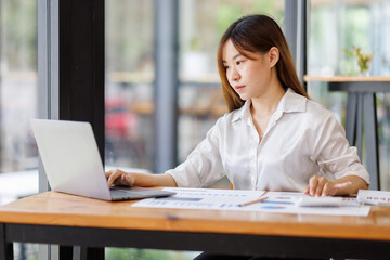 Fototapeta premium Businesswoman analyzing investment charts with calculator laptop. Accounting and technology in the office. Asian Business using laptop accountant Documents data partner deal in the workplace