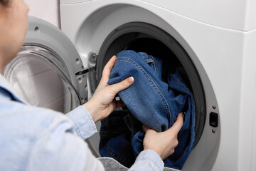 In laundry room, female person loads dirty laundry items into the washing machine. Woman in...