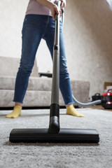 house cleaning concept. a close-up photo of a girl's legs and a vacuum cleaner brush. the girl...